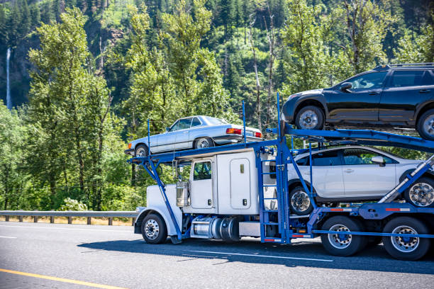 Industrial big rig white day cab car hauler semi truck tractor transporting cars on the hydraulic two level semi trailer driving on the one way highway road in green Columbia Gorge Recreation area